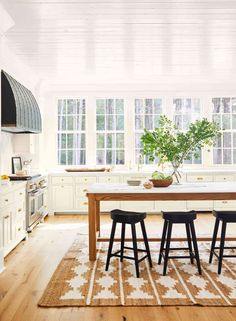 a kitchen with wooden floors and white walls, an island table surrounded by stools