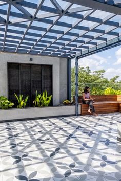 a woman sitting on a bench under a pergolated roof next to a planter