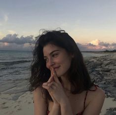 a woman sitting on the beach with her finger in her mouth