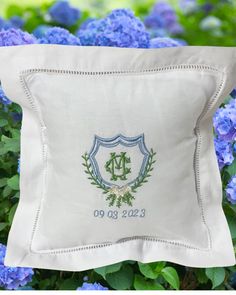 a white pillow sitting on top of blue hydrangea flowers in front of a green leafy bush