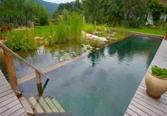 an outdoor pool surrounded by wooden decking next to a lush green field and pond