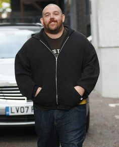 a man standing in front of a white car wearing a black hoodie and jeans