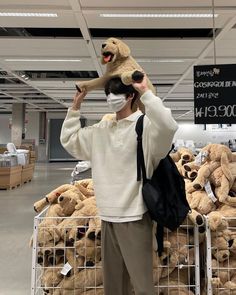 a man holding a teddy bear on his head while standing in front of a pile of stuffed bears