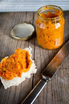 a jar of orange sauce next to a knife on a wooden table