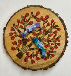 two colorful birds sitting on top of a wooden tree slice with red and blue leaves