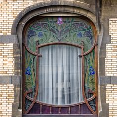 an ornate window on the side of a brick building with curtains and flowers in it