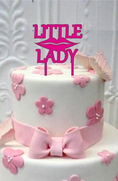 a three tiered cake decorated with pink and white fondant flowers, butterflies and a kiss on top