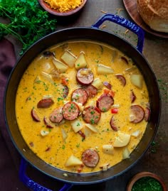 a pan filled with potatoes and sausages on top of a table next to bread