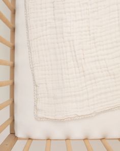 a baby crib with a white blanket and wooden slats on the bottom half