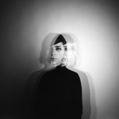 a black and white photo of a woman's face with long hair in front of a wall