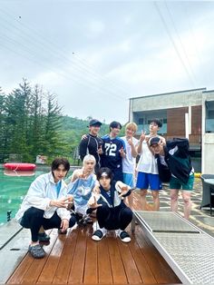 a group of young men standing on top of a wooden dock next to a lake