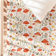 a white sheet with red mushrooms and flowers on it is next to a crib