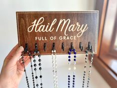 a wooden sign with beads hanging from it's sides and the words hail mary full of grace