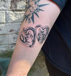 a person with a tattoo on their arm holding up a heart shaped photo frame and two cats