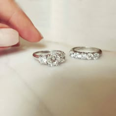 two diamond rings are being held by someone's hand while they sit on a white surface