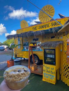 a person holding up a bowl of food in front of a yellow truck that says the sunrise shack