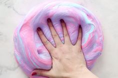 a person's hand on top of a pink and blue doughnut