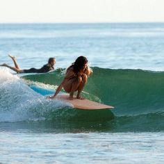 two people on surfboards in the ocean, one is riding a wave while the other is laying down