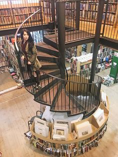 a woman standing on the top of a spiral staircase in a library filled with books