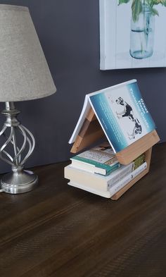 a stack of books sitting on top of a wooden table next to a lamp and painting