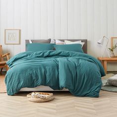 a bed with blue comforter and pillows in a white room next to pictures on the wall