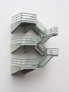 three metal staircases on the side of a white wall with no people in them