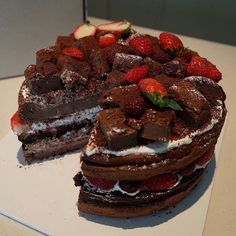 a chocolate cake with strawberries on top is cut in half and served on a platter