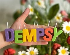 the word dempsy spelled out with small candles in front of some daisies