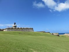 a grassy field with a statue on top of it and the ocean in the background