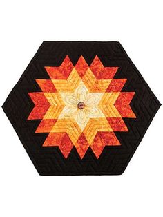 an orange and black star quilted on top of a white wall with a flower in the center