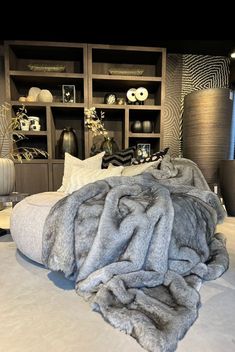 a large bed covered in grey fur next to shelves filled with vases and other decorative items