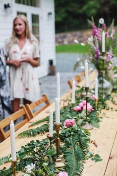 a long table topped with lots of flowers and candles next to two people standing in the background