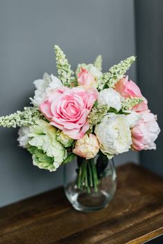 a vase filled with lots of pink and white flowers on top of a wooden table