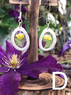 a pair of earrings with flowers on them sitting on top of a wooden stand next to a purple flower