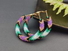 ✔️ Enhance your boho and hippie style with these exquisite handmade beaded hoop earrings. Made from high-quality glass materials, these earrings feature a stunning combination of green and purple beads that are meticulously handcrafted to create a unique and eye-catching design. With a size of 1.6 inches, they are the perfect accessory to add a touch of bohemian charm to your everyday outfits or special occasions. ✔️ Highlights: 1. Handmade Item: These hoop earrings are lovingly handmade, ensuri Beaded Hoop Earrings Native American, Earrings Native American, Hippie Fashion, Purple Beads, Earring Stand, Earrings Bohemian, Beaded Hoop Earrings, Bohemian Earrings, Free Spirited