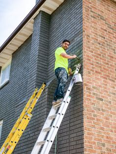 a man on a ladder painting the side of a brick building