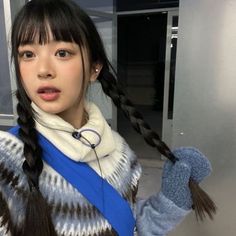 a girl with long black hair wearing a blue and white sweater holding up her hand