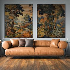 two paintings hang on the wall above a couch in a living room with hardwood floors