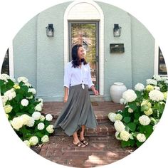 a woman standing in front of a door wearing a white shirt and gray skirt with flowers around her