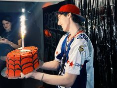 a man holding a cake with a candle in it and wearing a red hat on his head