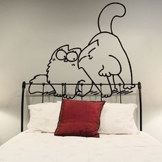 a cat and dog sticker on the wall behind a metal bed frame with red pillows