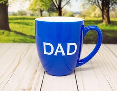 a blue coffee mug with the word dad written on it sitting on a wooden table