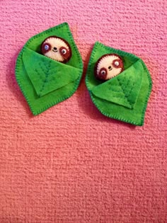 two small stuffed animals in green cloths on a pink surface, one with eyes and the other without