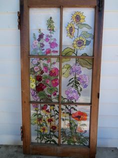 a window with flowers painted on the glass and wood frame, in front of a white house