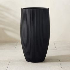 a large black vase sitting on top of a white tile floor next to a wall