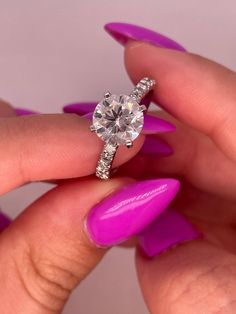 a woman's hand holding a pink manicured nail with a diamond ring on it