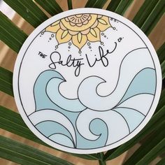 a round sticker with the words salty life on it next to a palm leaf