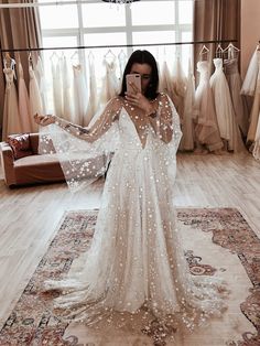 a woman standing in front of a wedding dress with long sleeves and sequins on it