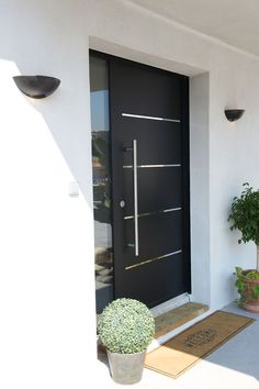 a black front door with two potted plants next to it and an entrance mat