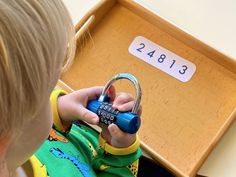 a little boy holding a blue padlock in front of a box with numbers on it